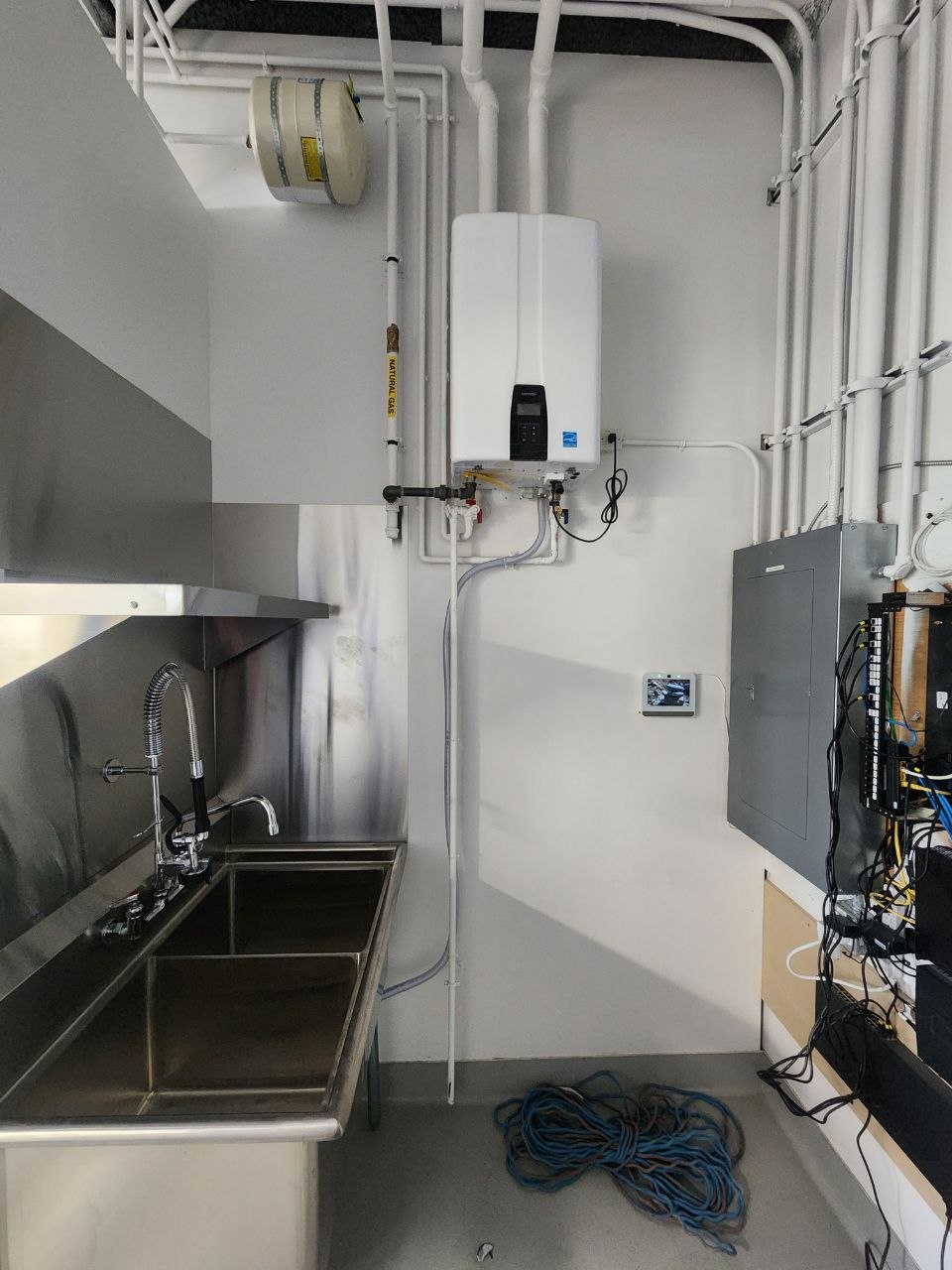 Gas-fired tankless hot water system installed beside a commercial three-compartment sink in a Calgary bakery