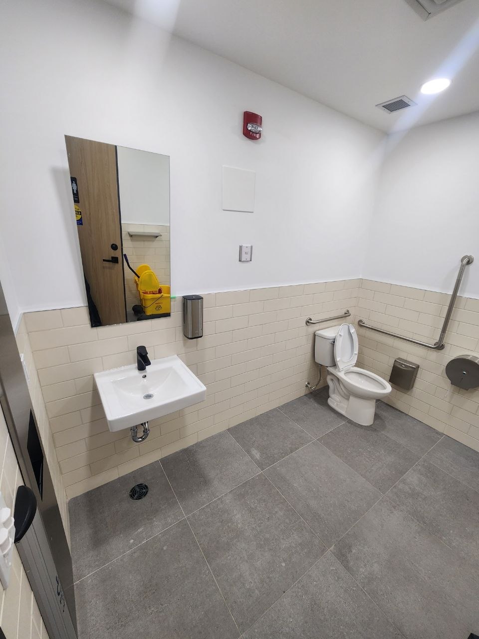 Accessible commercial washroom with a toilet, grab bars, wall-mounted sink and floor drain
