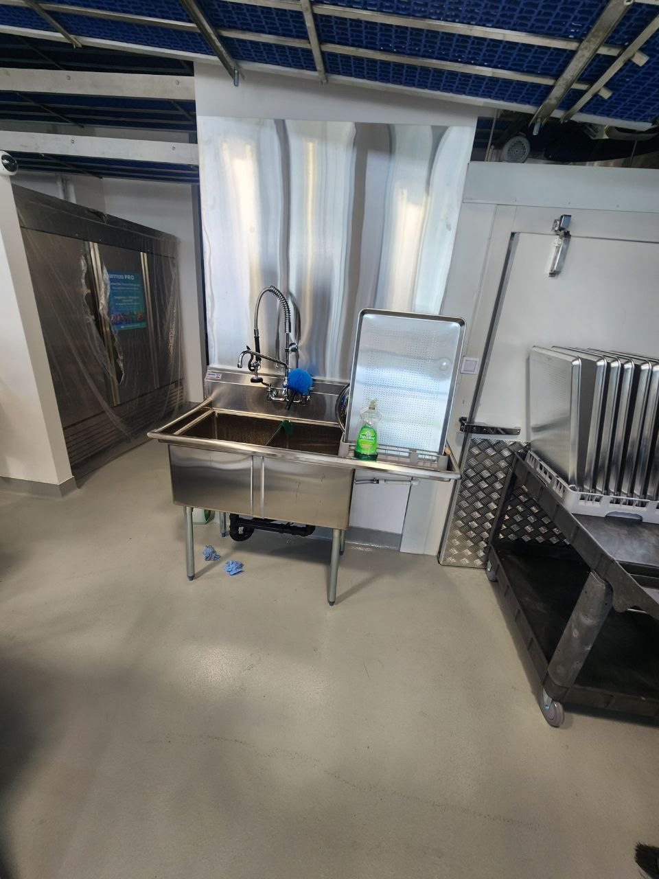 Stainless commercial wash station beside bakery racks and a cold storage door